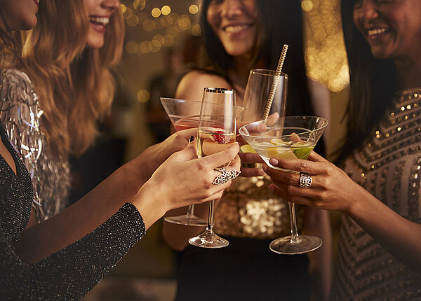 Nahaufnahme von einer Gruppe junger Frauen in glitzernden Partyoutfits, die gerade mit Cocktails anstoßen.