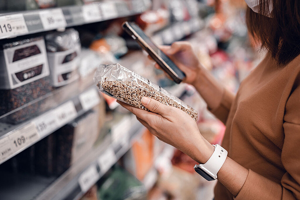 Eine Frau im Supermarkt überprüft die Zutatenliste eines Lebensmittels, das sie in der Hand hält.